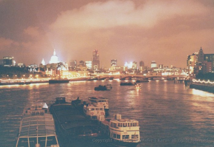 London brightly lit at night, with barges and boats along the Thames