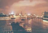 London brightly lit at night, with barges and boats along the Thames